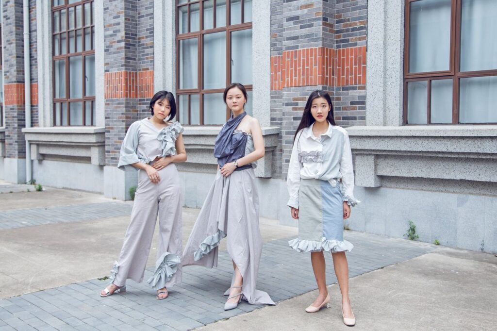 Three fashionable women pose confidently outdoors in stylish urban attire.