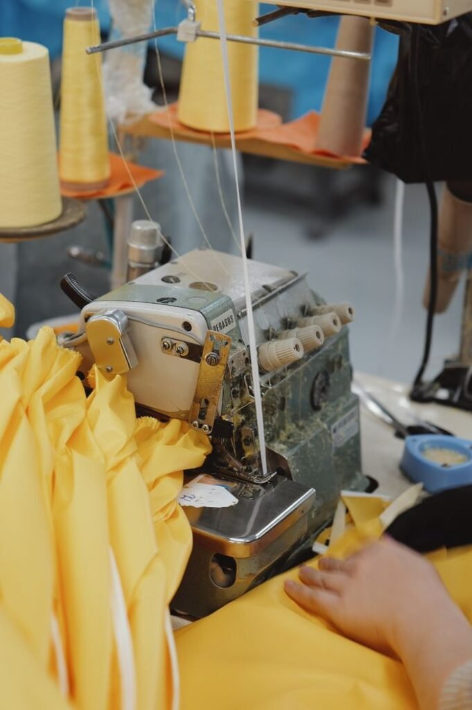 Close-up of hands working with a sewing machine and bright yellow fabric in a textile workshop.