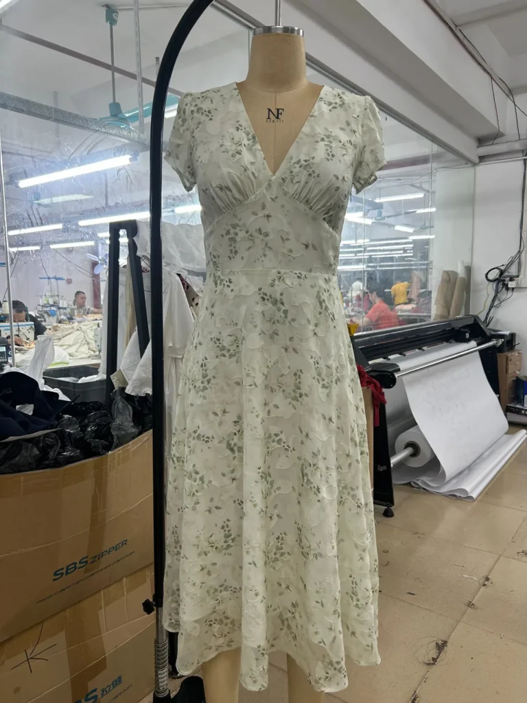 Light green floral V-neck midi dress displayed on a mannequin in the Mugekoo garment workshop.