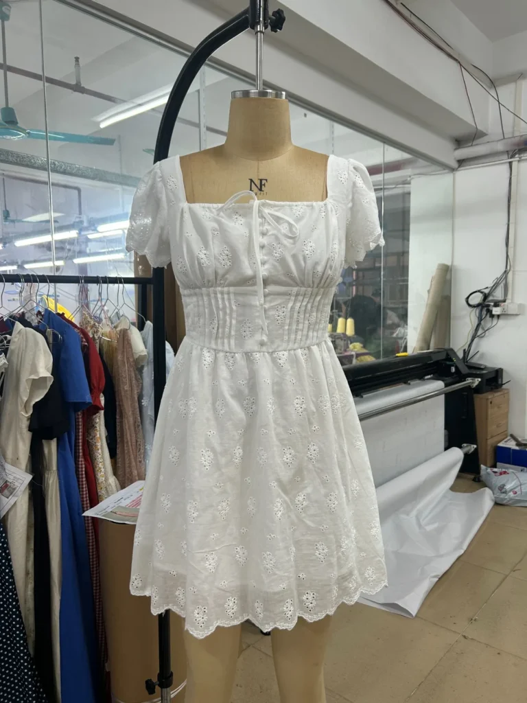 White mini dress with a square neckline, puff sleeves and scalloped hem on a mannequin.
