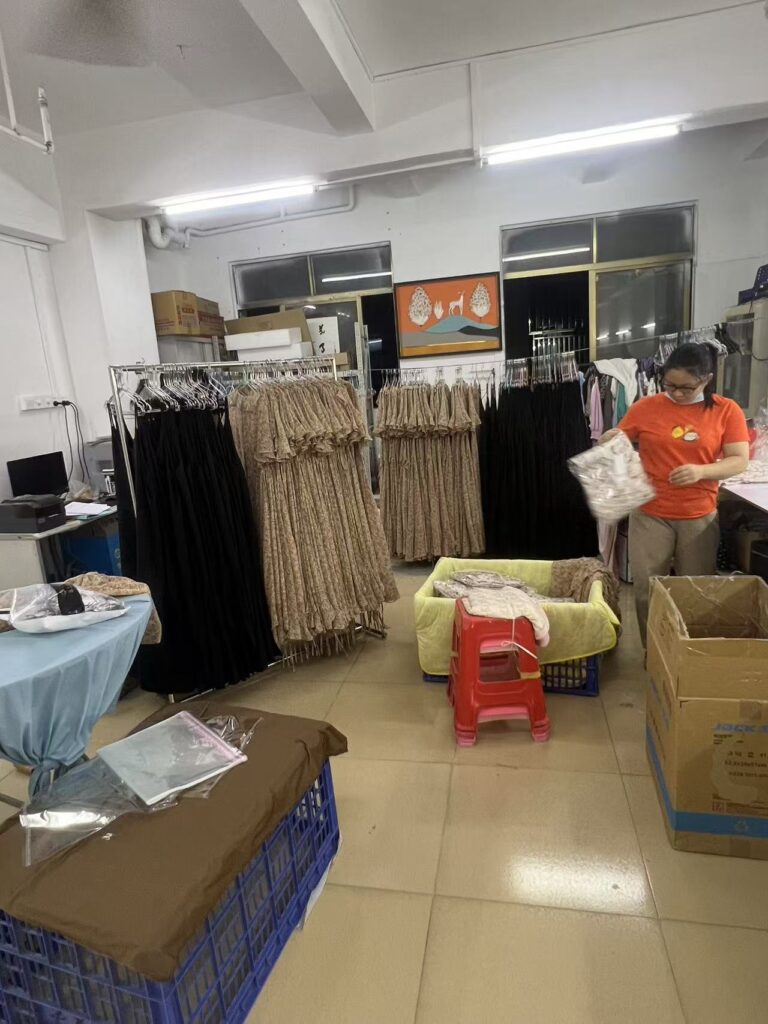 Worker packing garments beside racks of black and beige clothing