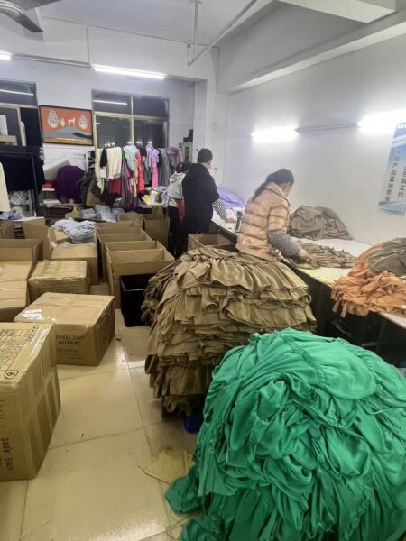 Workers sorting green and tan garments on tables beside packing cartons