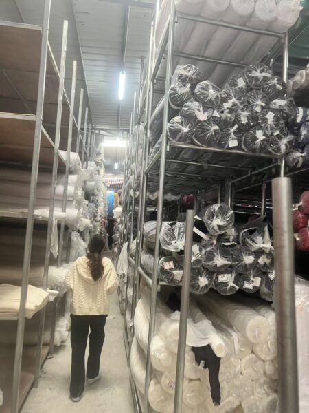 Person walking between tall metal racks holding black and white fabric rolls