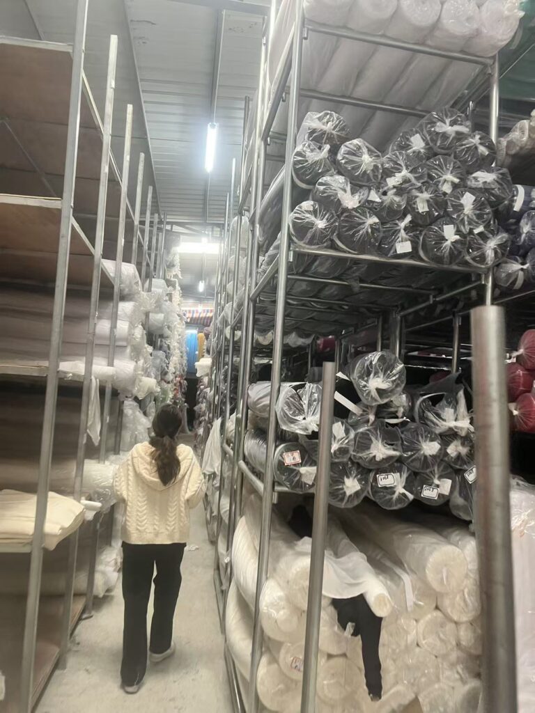 Person walking between tall metal racks holding black and white fabric rolls