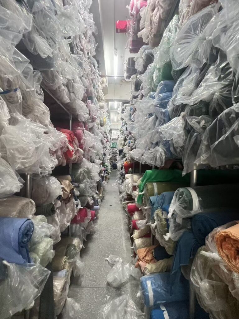 Narrow aisle between tall shelves filled with wrapped fabric rolls in assorted colors