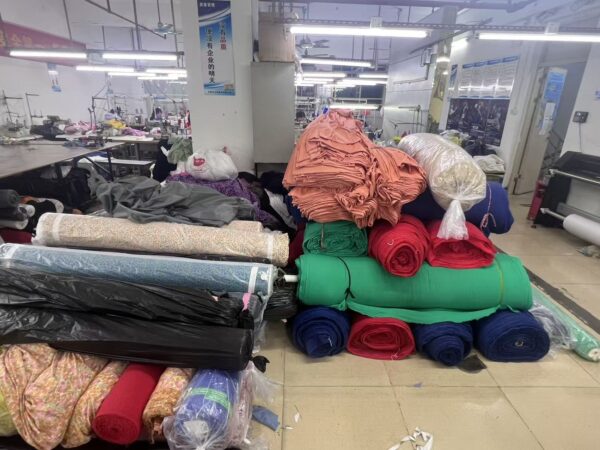 Stacks of green, red, navy and printed fabric rolls beside cut fabric bundles
