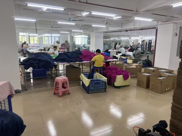 Workers handling garments at finishing tables beside packing boxes