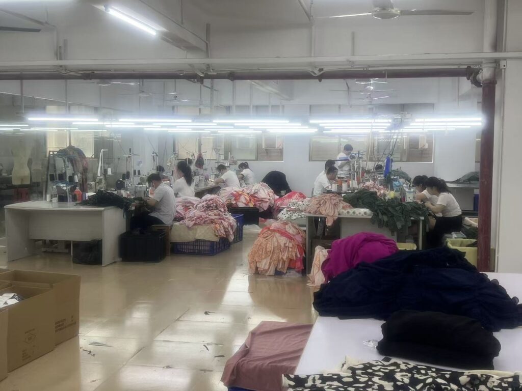 Workers behind tables piled with colorful garment bundles in a sewing workshop