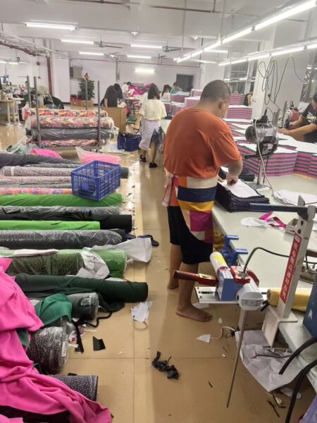 Worker using a pressing table beside green, pink and printed fabric rolls