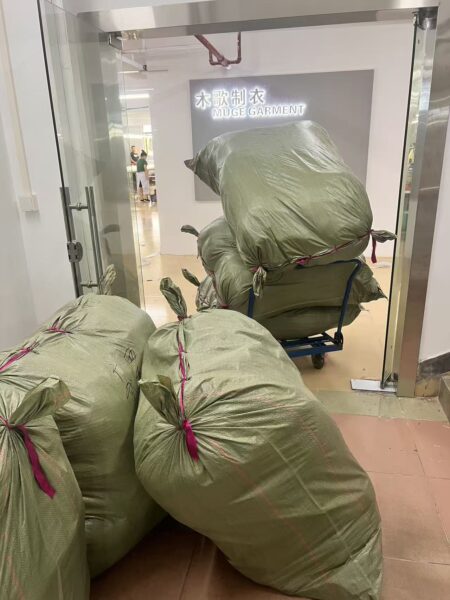 Large tied green storage bags beside a trolley at the workshop entrance