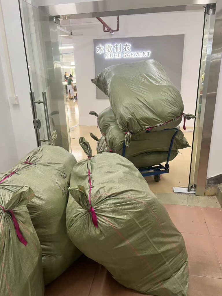 Large tied green storage bags beside a trolley at the workshop entrance