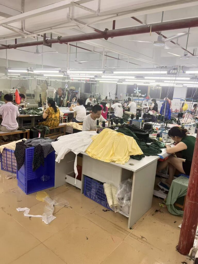 Workers handling yellow and white garments at sewing workshop tables