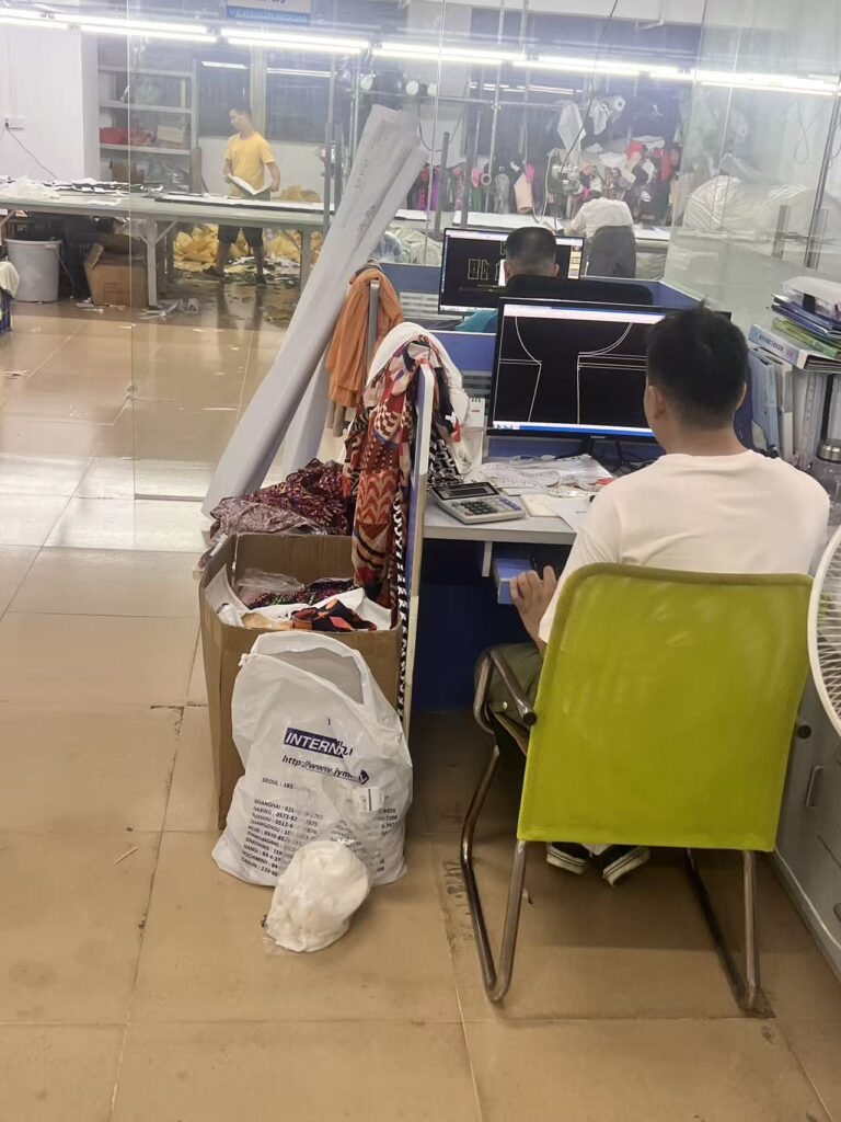 Staff member viewing digital garment patterns beside hanging fabric and clothing samples
