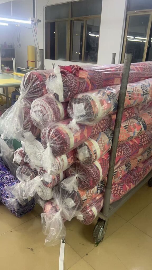 Red, purple and multicolored printed fabric rolls stacked on a metal trolley