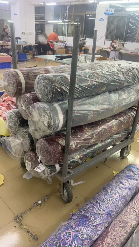 Plastic wrapped printed fabric rolls stacked horizontally on a wheeled trolley