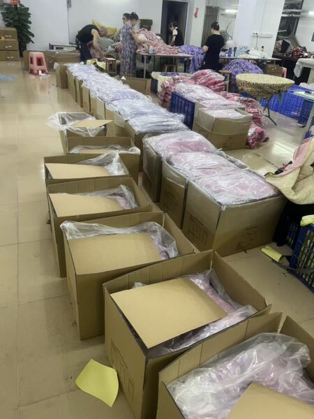 Open cartons containing plastic wrapped garments beside packing tables
