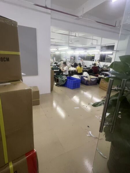 View past stacked cartons into a sewing area with workers and garment baskets