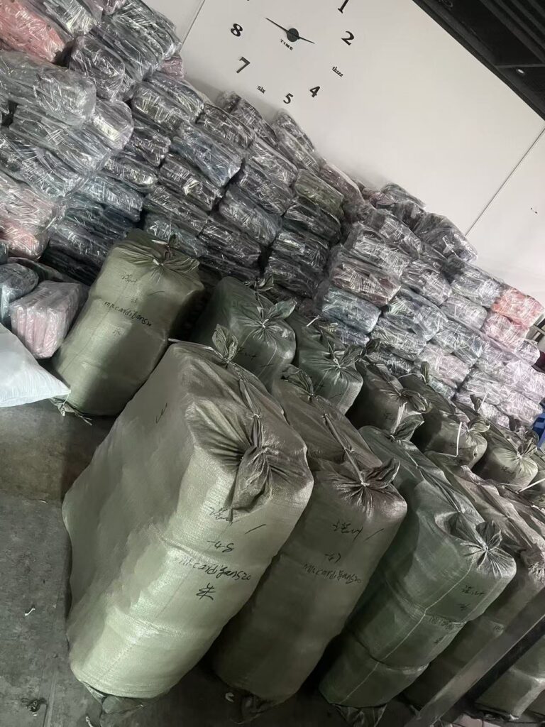 Stacks of plastic wrapped garments behind large green storage bags