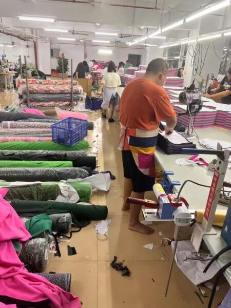 Worker pressing a garment at a finishing station beside fabric rolls