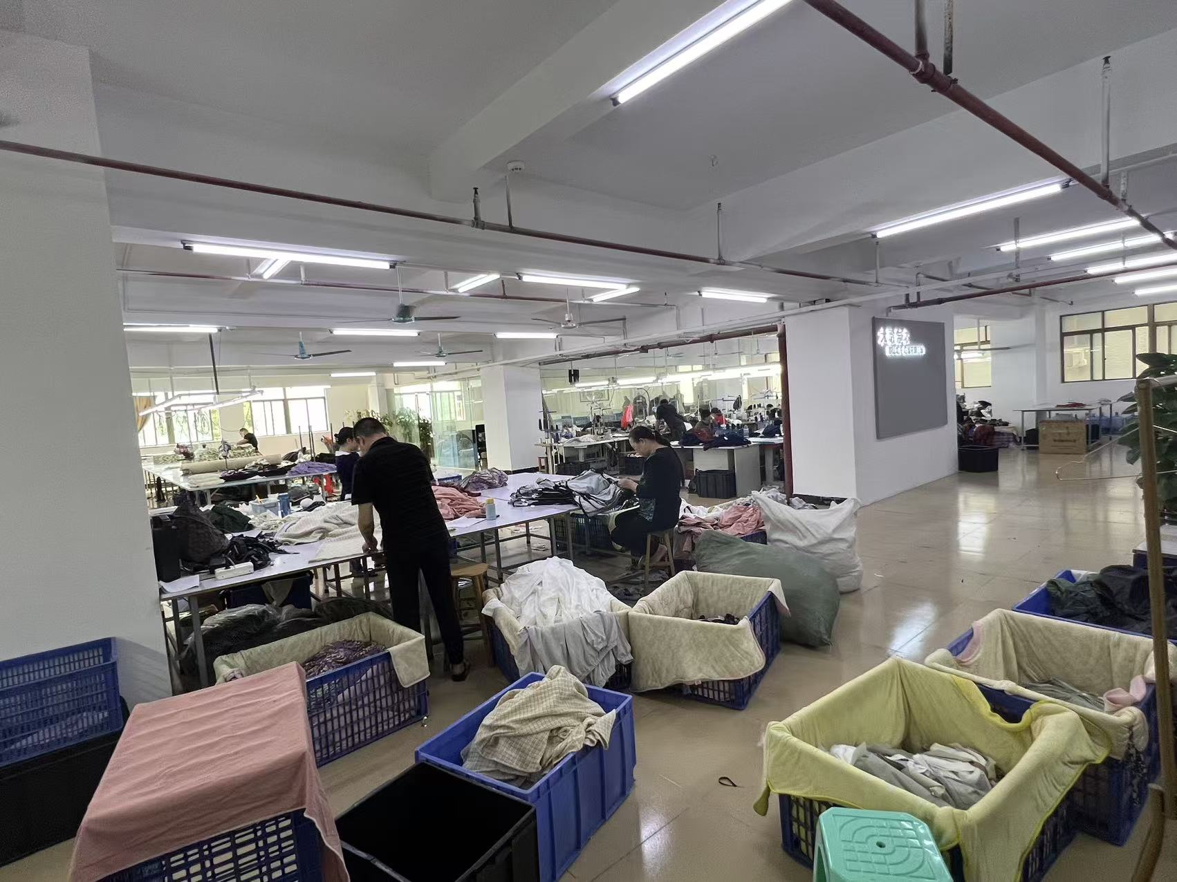 Workers and garment bins arranged around tables in a clothing production area