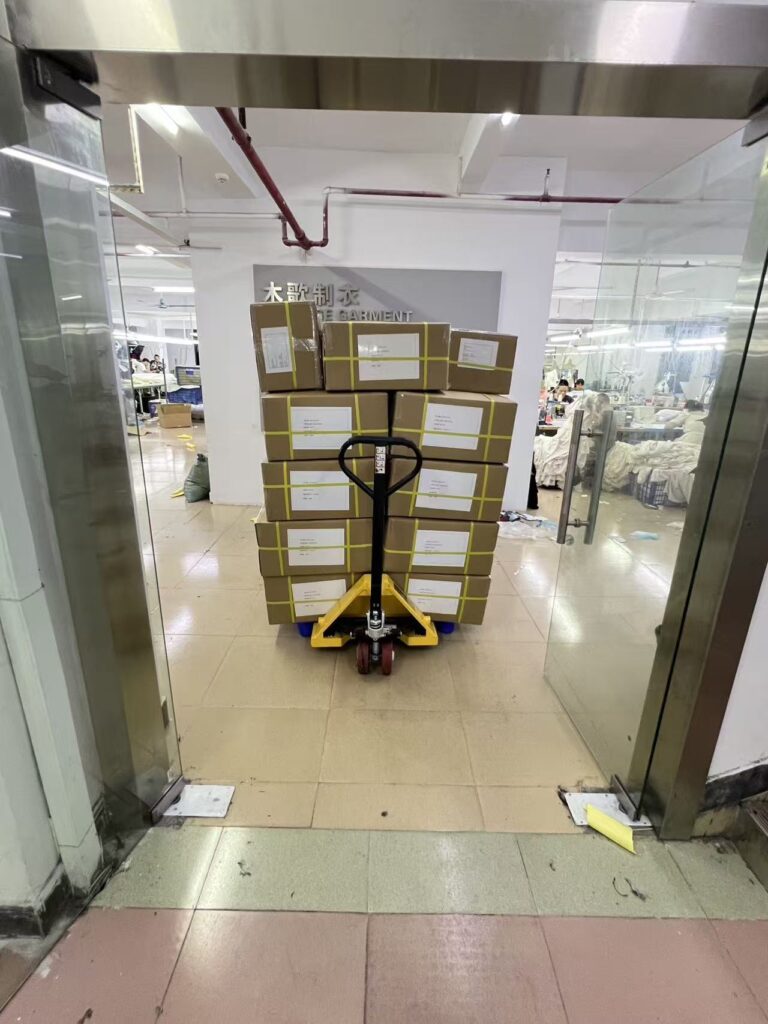 Stacked sealed cartons on a yellow pallet jack at the workshop entrance