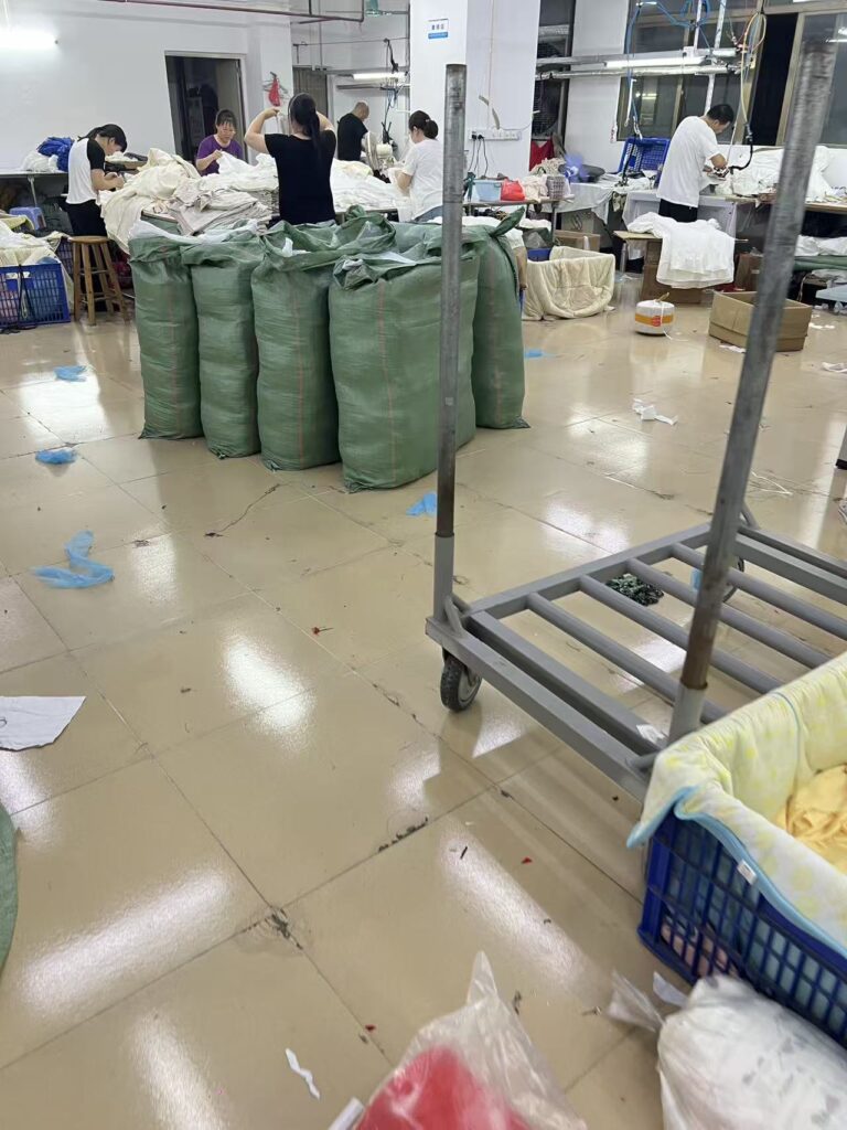 Large green storage bags and a metal trolley beside garment work tables