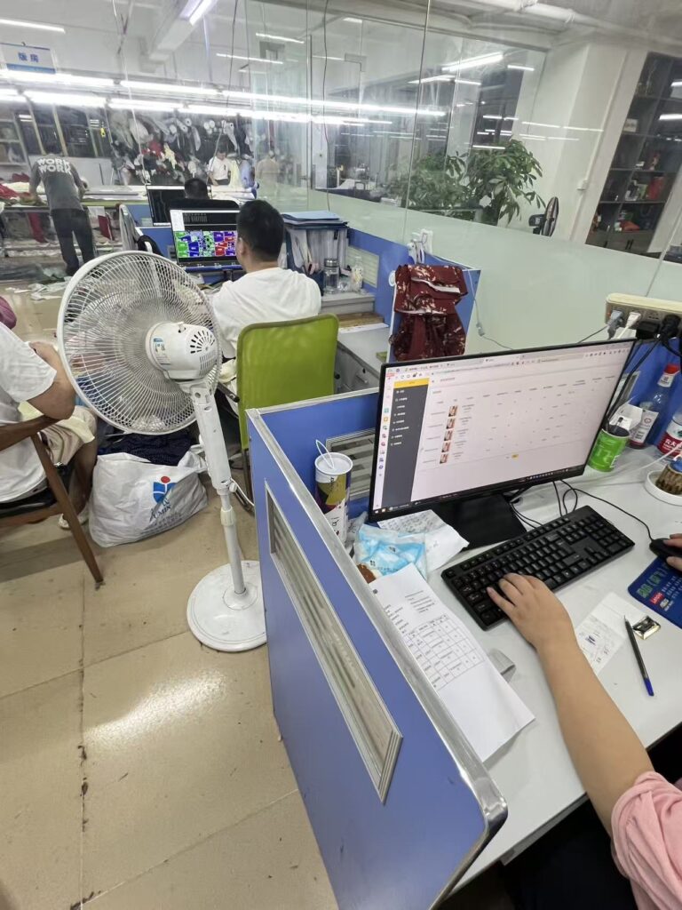 Staff working at computer desks beside a glass partition in a garment workshop