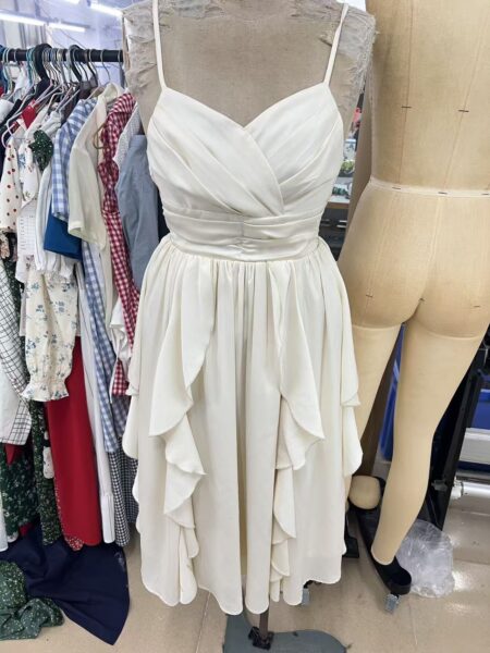 Ivory thin strap dress with a ruched bodice and cascading skirt panels on a dress form
