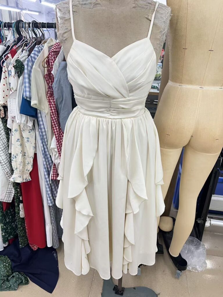 Ivory thin strap dress with a ruched bodice and cascading skirt panels on a dress form