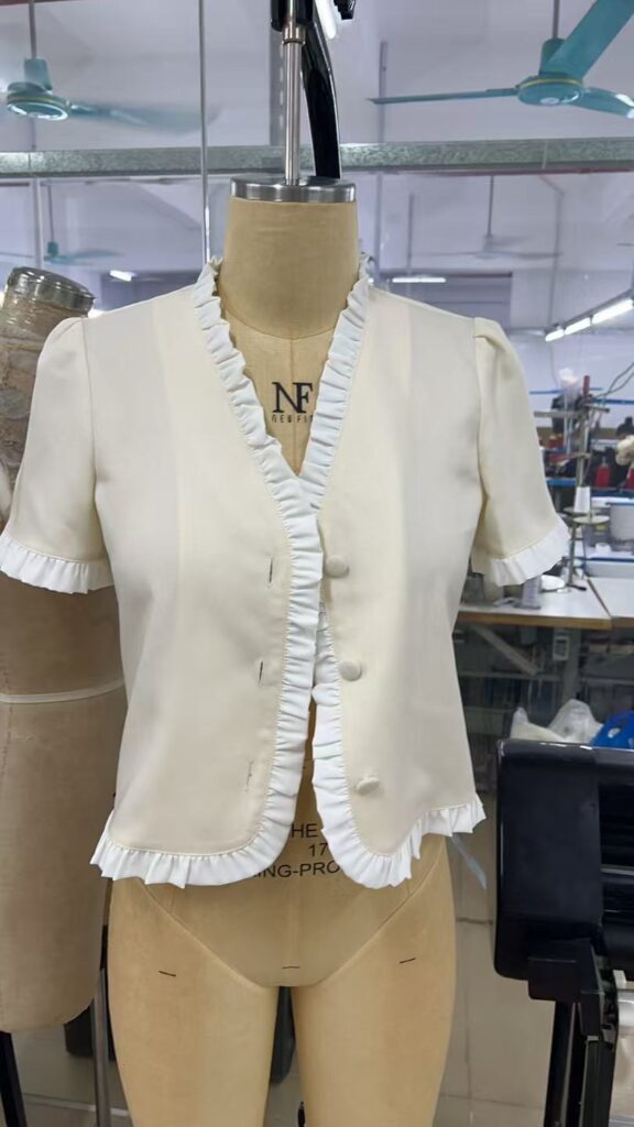 White short sleeve button front jacket with ruffled neckline and hem on a dress form