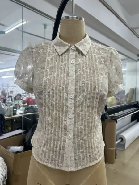 Cream embroidered blouse on a dress form with puff sleeves, a pointed collar and a pleated button front.