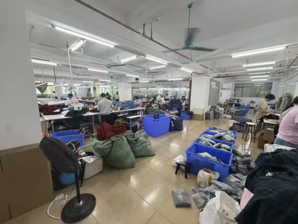 Wide view of a garment production floor with sewing stations, blue bins and bundled materials.